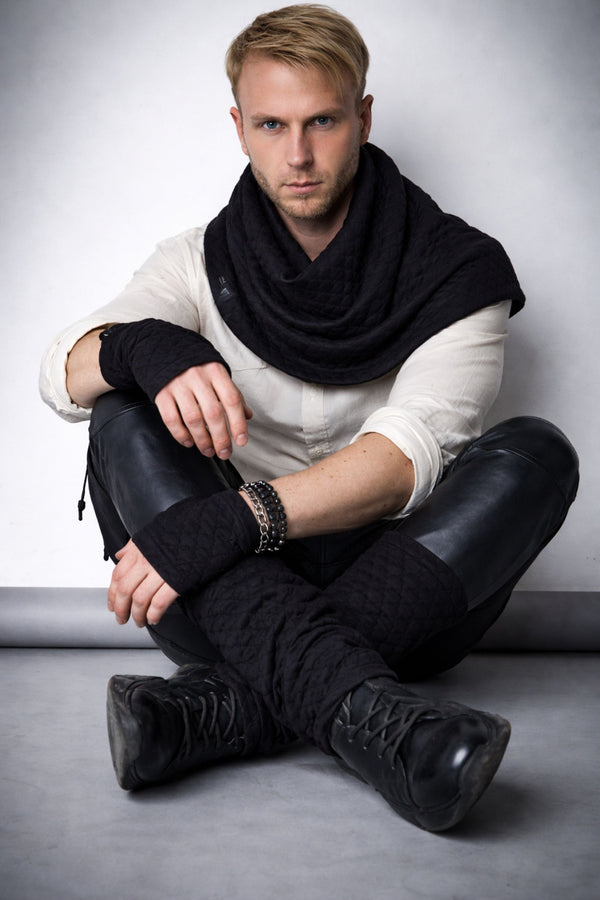 Black quilted scarf with structured drape on male model, styled with white shirt and leather pants, brutal minimal techwear look, seated pose