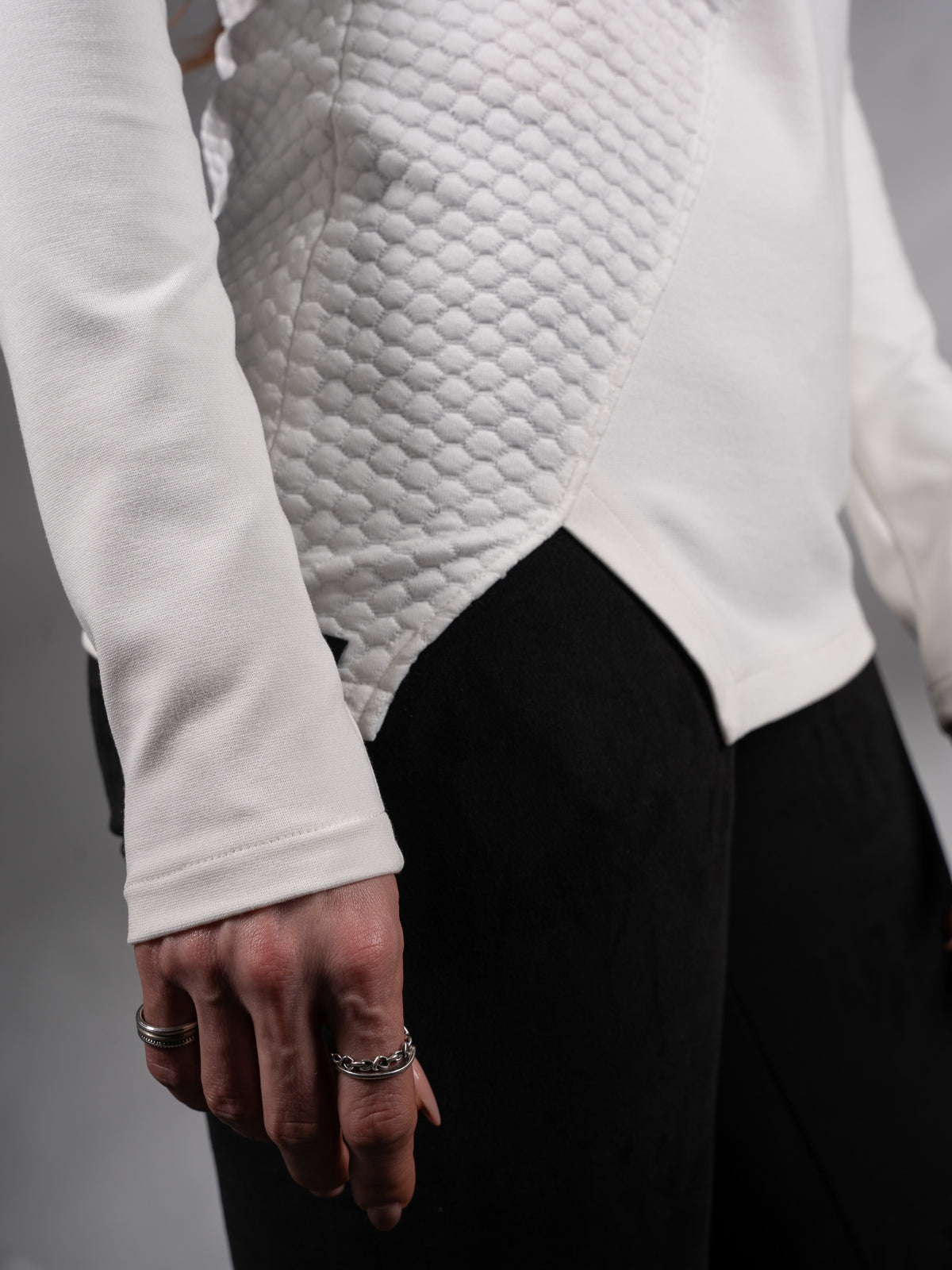 Close-up of asymmetric hem and textured panel on white sweater – ZOLNAR